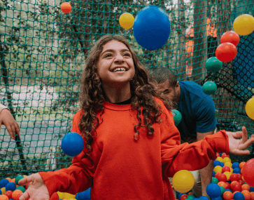 A child looking excited as they play in a colourful ball pit